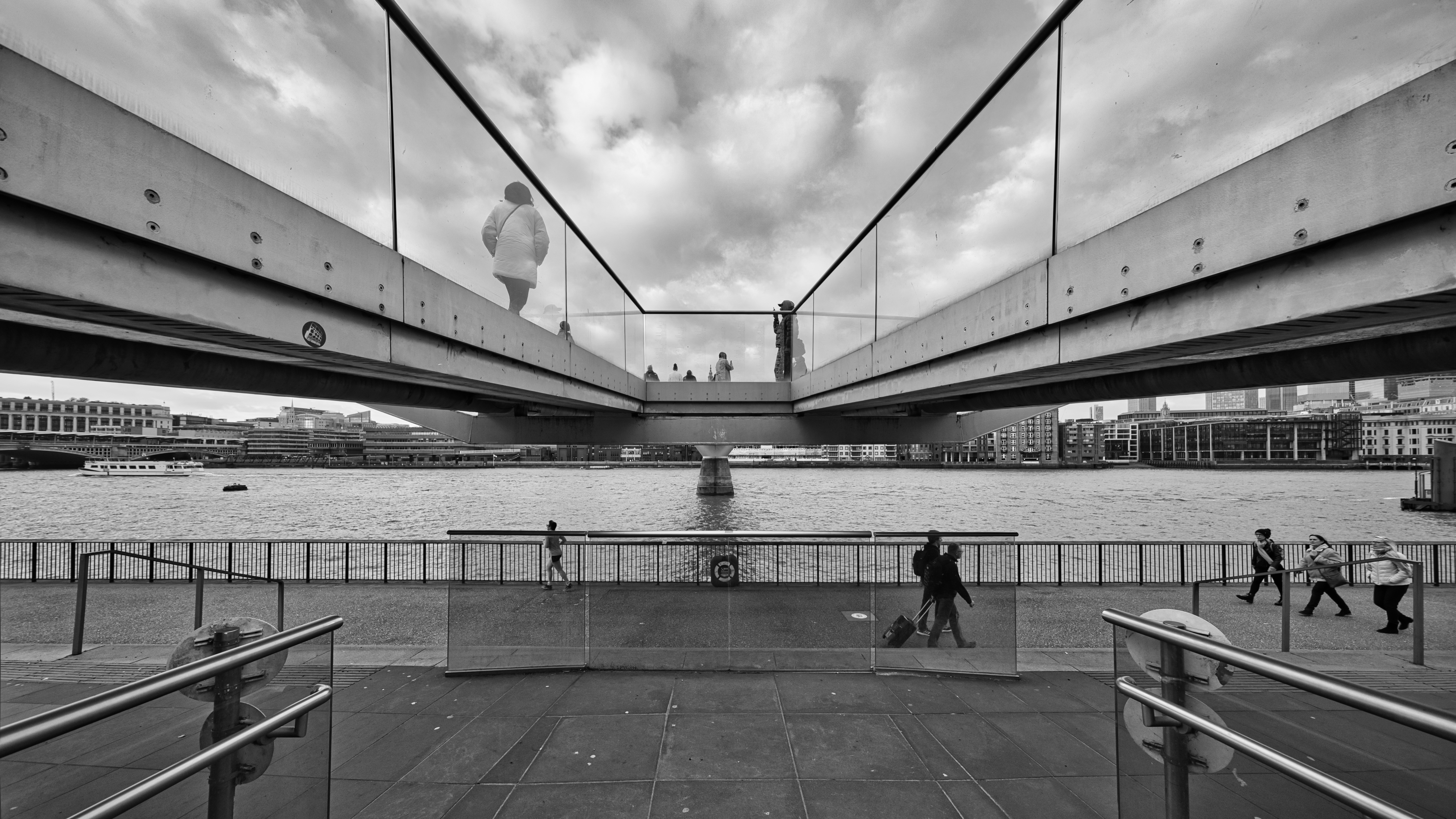People walking along the South Bank beside the Thames, with the Millennium Bridge stretching across the river.